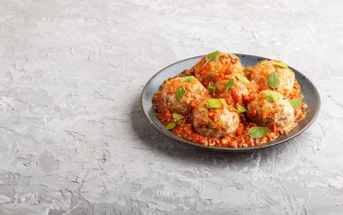 Pork meatballs with tomato sauce, oregano leaves, spices and herbs on blue ceramic plate on a gray