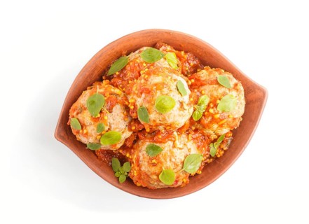 Pork meatballs with tomato sauce, oregano leaves, spices and herbs in clay bowl isolated on white