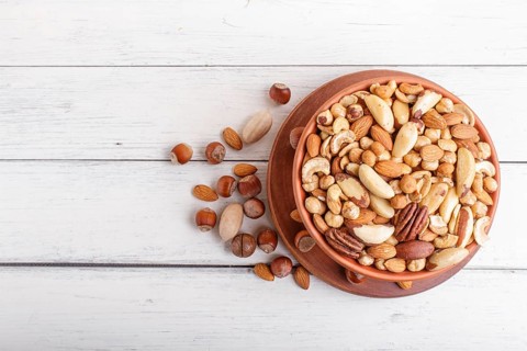 Mixed different kinds of nuts in ceramic bowl on white wooden background with copy space. hazelnut,