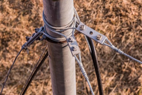 Top down view of wire cables attached to metal pole with brown grass blurred in background in South