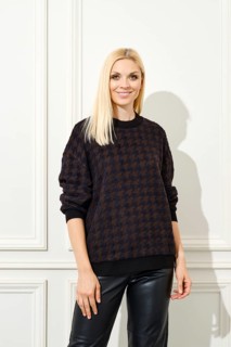 Cheerful woman stands against a white paneled wall, adorned in a stylish houndstooth patterned