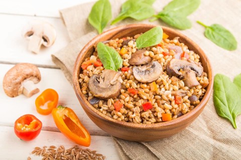 Spelt (dinkel wheat) porridge with vegetables and mushrooms in wooden bowl on a white wooden