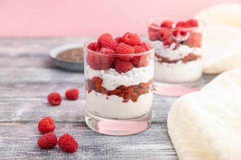 Yogurt with raspberry, goji berries and chia seeds in glass on gray wooden background and linen