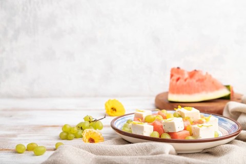 Vegetarian salad with watermelon, feta cheese, and grapes on blue ceramic plate on white wooden