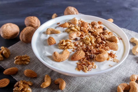 White plate with greek yogurt, granola, almond, cashew, walnuts on black wooden background. close