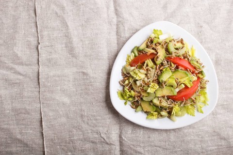 Vegetarian salad of celery, germinated rye, tomatoes and avocado on linen tablecloth, top view,