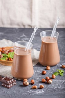 Organic non dairy hazelnut chocolate milk in glass and wooden plate with hazelnuts on a black