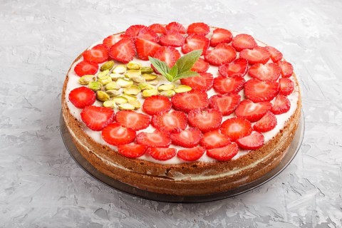 Homemade cake with yoghurt cream, strawberry and pistachio on a gray concrete background. side