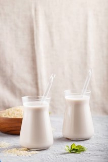 Organic non dairy rice milk in glass and wooden plate with rice seeds on a gray concrete background