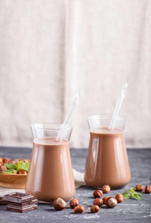 Organic non dairy hazelnut chocolate milk in glass and wooden plate with hazelnuts on a black