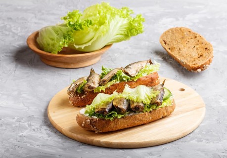 Sprats sandwiches with lettuce and cream cheese on wooden board on a gray concrete background. side