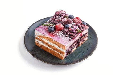 Berry cake with milk cream and blueberry jam on blue ceramic plate isolated on white background.