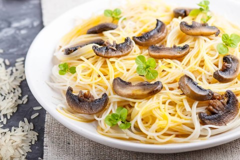 Rice noodles with champignons mushrooms, egg sauce and oregano on white ceramic plate on a black