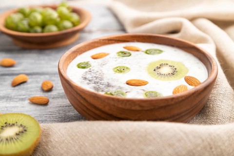 Yogurt with kiwi, gooseberry, chia and almonds in wooden bowl on gray wooden background and linen
