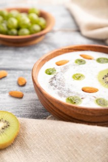 Yogurt with kiwi, gooseberry, chia and almonds in wooden bowl on gray wooden background and linen