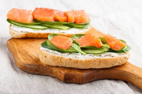 Smoked salmon sandwiches with cucumber and spinach on wooden board on a linen background. side