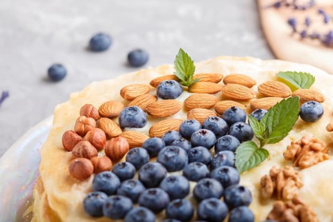 Homemade layered Napoleon cake with milk cream. Decorated with blueberry, almonds, walnuts,