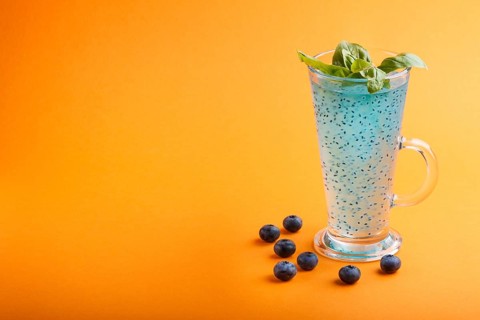 Glass of blueberry blue colored drink with basil seeds on orange background. Morninig, spring,