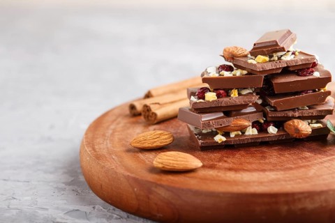 A pieces of milk chocolate with almonds and dried fruits on a brown wooden board on a gray concrete
