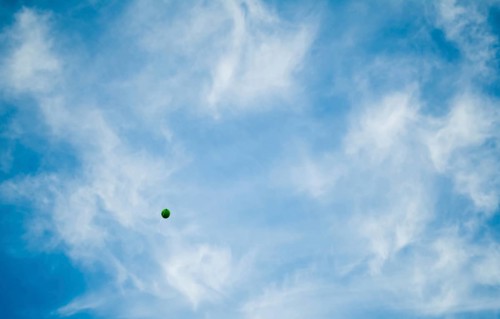 Green balloon from a St. Patrick's Day festival floating away in a blue sky filled with wispy white