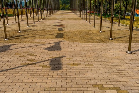 Shadows of flags on brick walkway between rows of chrome flagpoles in South Korea