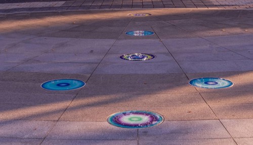 Arrow of round glass tiles of blue, purple, yellow and white inlaid in concrete sidewalk in public