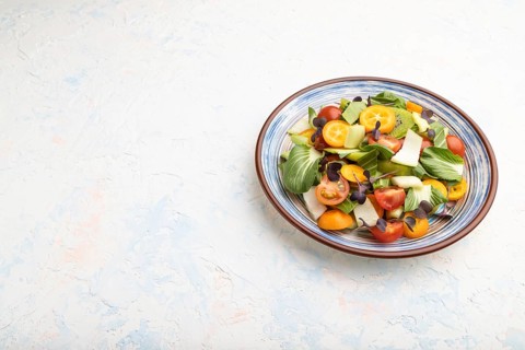 Vegetarian salad of pac choi cabbage, kiwi, tomatoes, kumquat, microgreen sprouts on a white