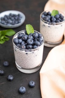 Yogurt with blueberry and chia in glass on black concrete background and orange linen textile. Side