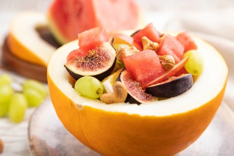 Vegetarian fruit salad of watermelon, grapes, figs, pear, orange, cashew on white wooden background