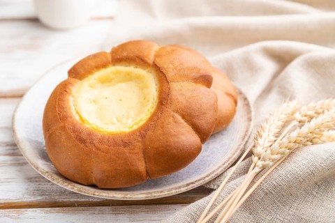 Sour cream bun with cup of coffee on a white wooden background and linen textile. Side view, close