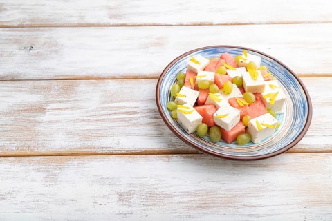 Vegetarian salad with watermelon, feta cheese, and grapes on blue ceramic plate on white wooden