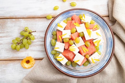 Vegetarian salad with watermelon, feta cheese, and grapes on blue ceramic plate on white wooden