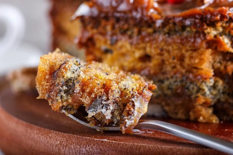 A piece of cake with caramel cream cutted with spoon on a wooden kitchen board and a cup of coffee,
