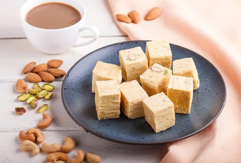 Traditional indian candy soan papdi in a blue ceramic plate with almond, pistache, cashew and a cup