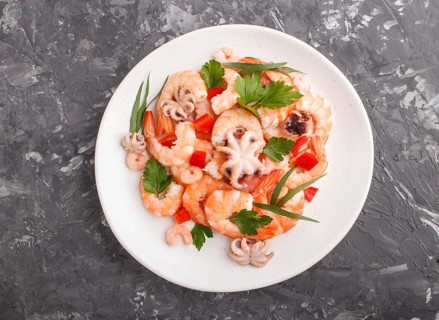 Boiled shrimps or prawns and small octopuses with herbs on white ceramic plate on a black concrete