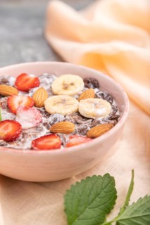 Chocolate cornflakes with milk, strawberry and almonds in ceramic bowl on gray concrete background