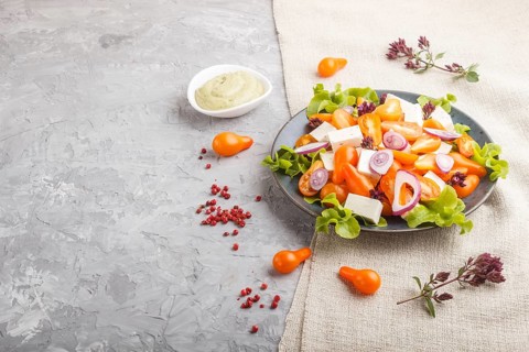 Vegetarian salad with fresh grape tomatoes, feta cheese, lettuce and onion on blue ceramic plate on