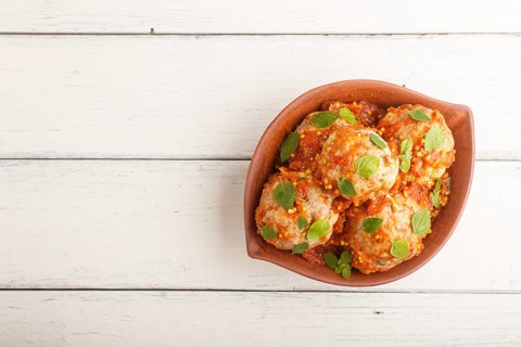 Pork meatballs with tomato sauce, oregano leaves, spices and herbs in clay bowl on a white wooden