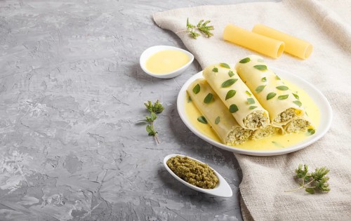 Cannelloni pasta with egg sauce, cream cheese and oregano leaves on a gray concrete background with