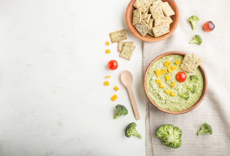 Green broccoli cream soup with crackers and cheese in wooden bowl on a white wooden background and