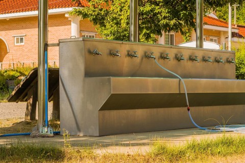Multifaceted public washing sink and water fountain with hose attached to faucet at edge of public
