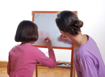 Two children are focused on drawing on a paper affixed to an easel with colorful markers, Youngs
