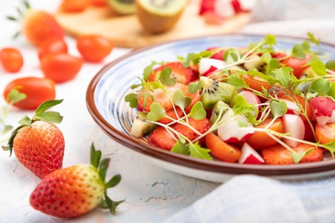 Vegetarian fruits and vegetables salad of strawberry, kiwi, tomatoes, microgreen sprouts on white