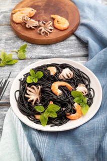 Black cuttlefish ink pasta with shrimps or prawns and small octopuses on gray wooden background and