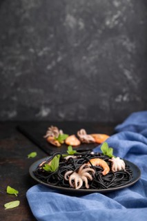 Black cuttlefish ink pasta with shrimps or prawns and small octopuses on black concrete background