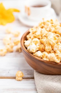 Popcorn with caramel in wooden bowl and a cup of coffee on a white wooden background and linen