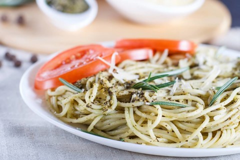 Spaghetti pasta with pesto sauce, tomatoes and cheese on a linen tablecloth. close up, selective