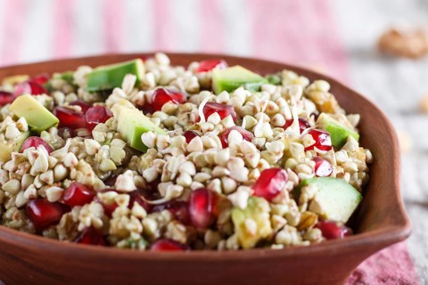 Salad of germinated buckwheat, avocado, walnut and pomegranate seeds in clay plate on white wooden