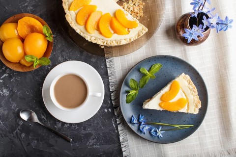 A piece of peach cheesecake on a blue ceramic plate with blue flowers and a cup of coffee on a