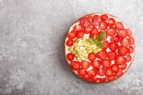 Homemade cake with yoghurt cream, strawberry and pistachio on a gray concrete background. top view.
